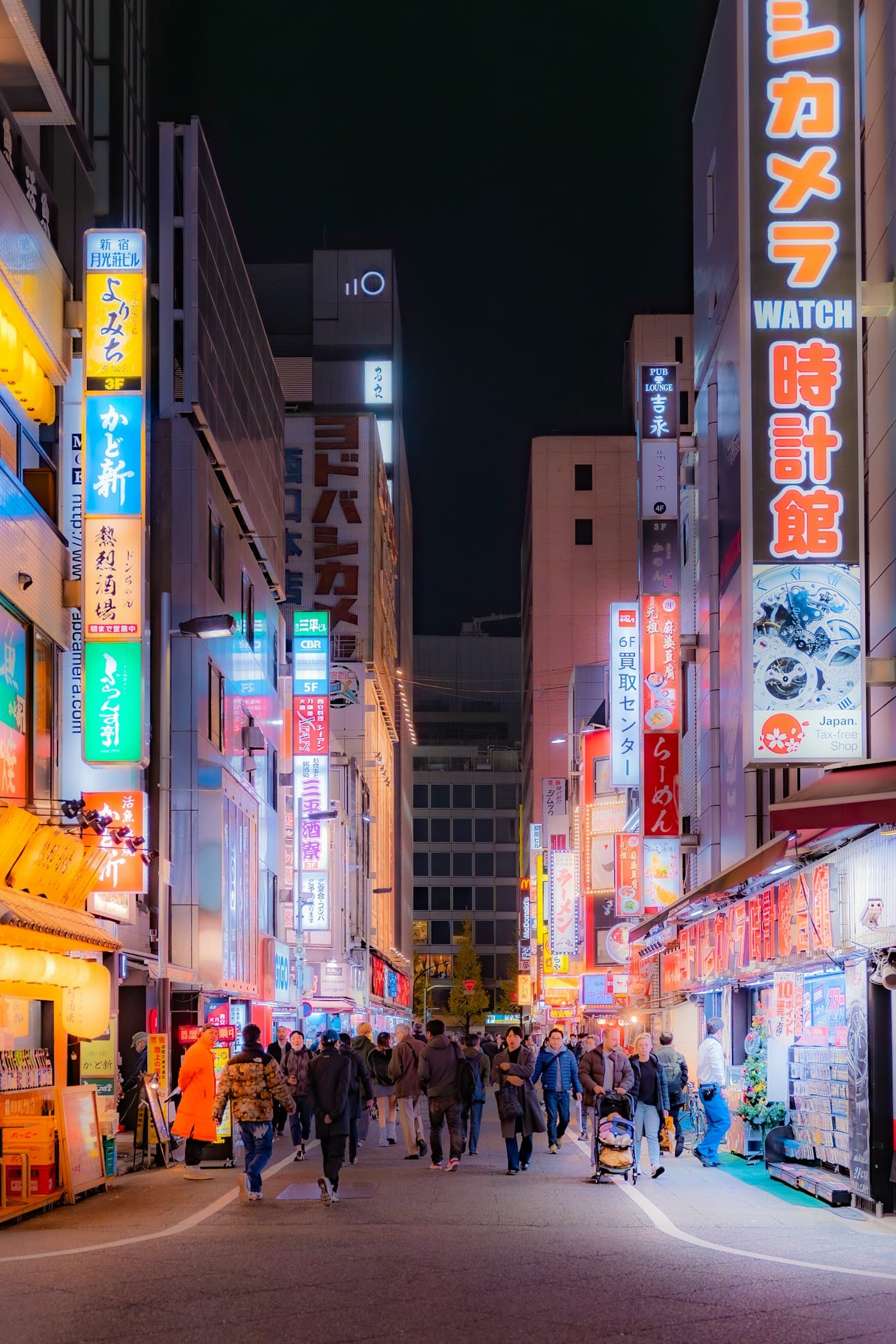 People exploring a brightly lit street in Shinjuku, Tokyo, at night